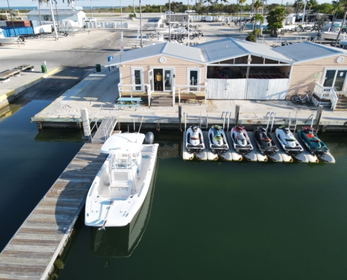 A stunning drone view of a boat and jet skis docked at a scenic marina in the Florida Keys, surrounded by crystal-clear turquoise waters.